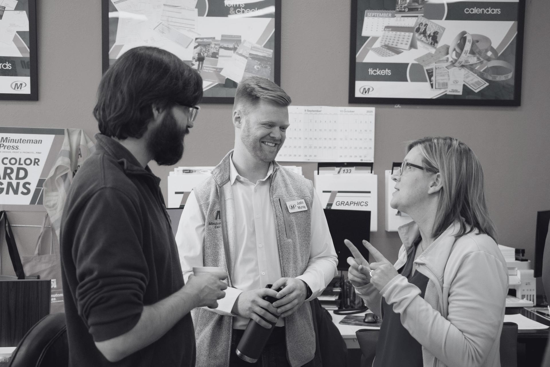 Justin on the floor of Minuteman Press, mid-conversation with two of his employees.