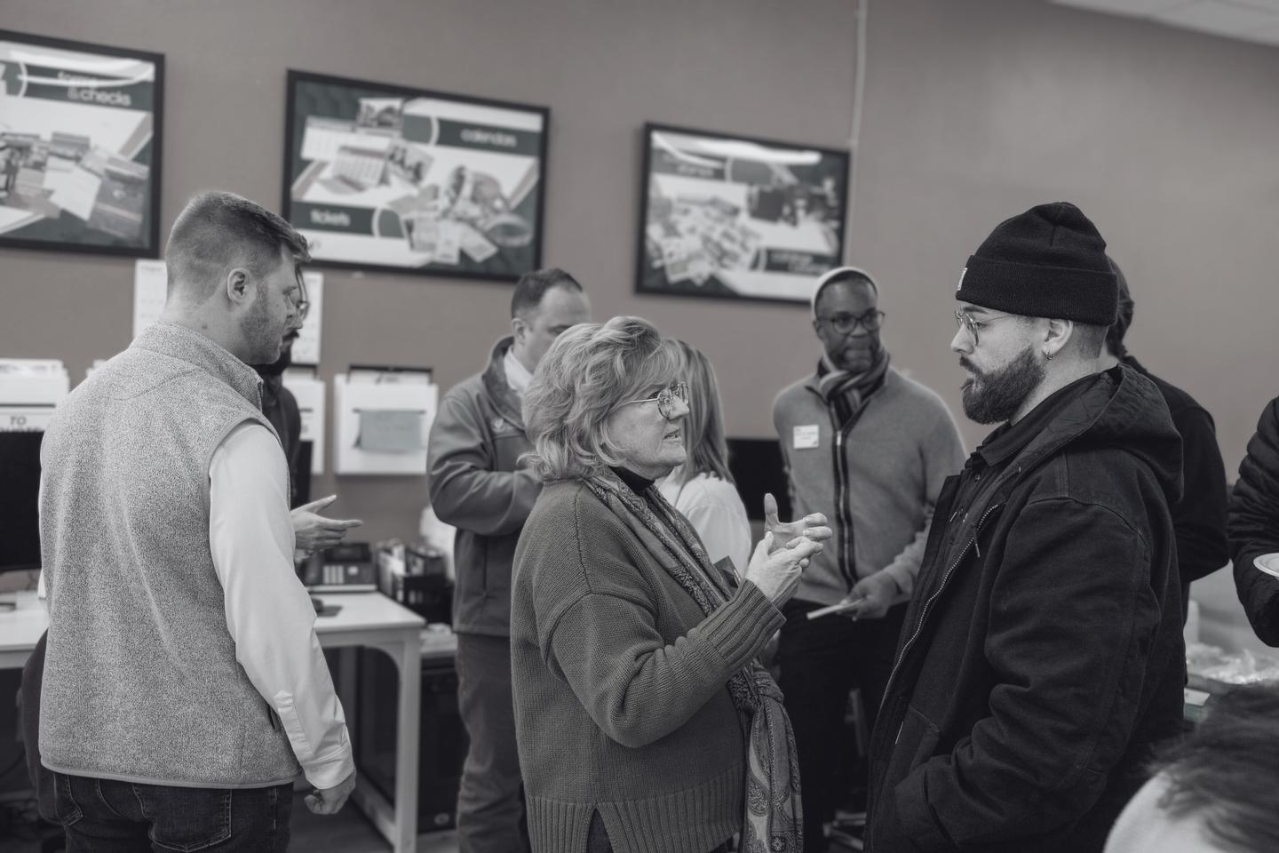 A circle of business owners in conversation at a networking event inside a print shop, several side discussions underway.